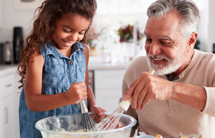 Grandfather making food with granddaughter in kitchen