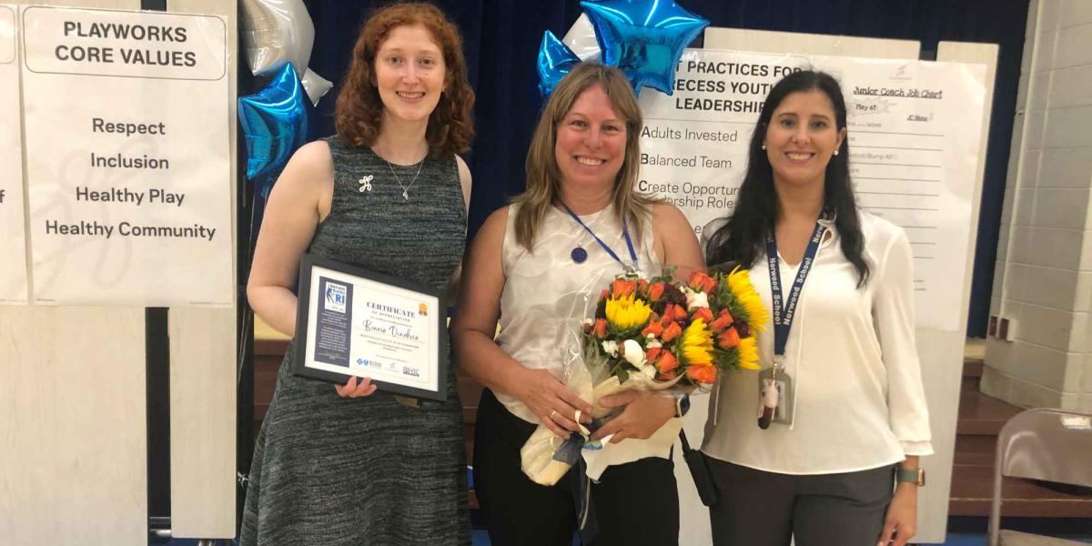 Jessi Jasper, Playworks New England Regional Partnerships Manager, presents a certificate of appreciation to Bonnie Donahue, a building/recess aide at Norwood Elementary School in Warwick, who was honored as a Recess Rocks in RI 2023 Recess Champion. At right is Principal Sabrina Antonelli.