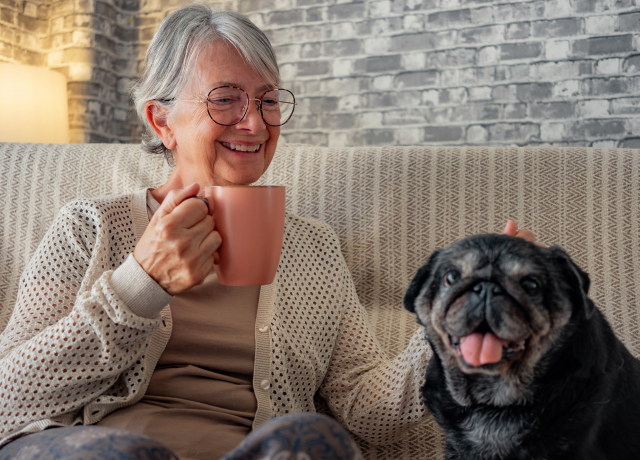 Senior woman drinking coffee on a couch with her dog