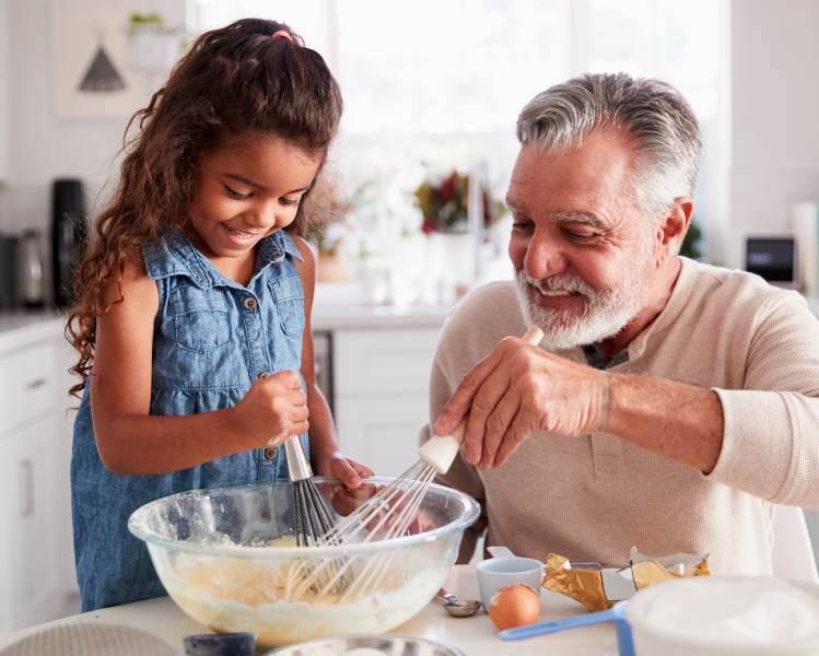 Photo of grandfather with granddaughter making food in the kitchen